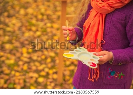 hands of a little artist girl with a brush and paints in autumn