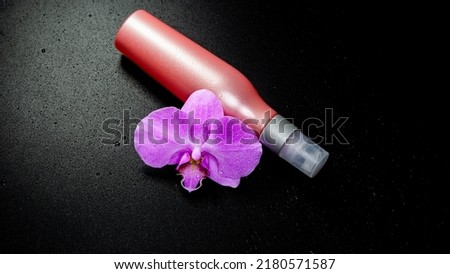  Isolated pink bottle for cosmetic, and purple orchid with drops on black background
