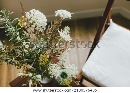 Wildflowers bouquet and wooden chair in rustic room. Summertime in countryside. Home simple eco decor Royalty-Free Stock Photo #2180576435