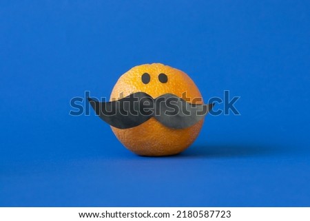 Photo of an orange with black mustache and eyes placed on a dark blue surface