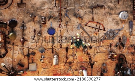 Old utensils are hung on the wall. Antique Junk. Clock, Pan, Meat grinder, Axe. Rusty Stuff. Brown Shabby Grungy Wallpaper. Flea Market Things in Israel