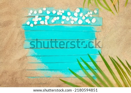 Turquoise boards with seashells on beach sand and palm tree. Vacation, travel concept. Copy space
