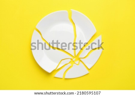 Pieces of broken ceramic plate on yellow background, flat lay