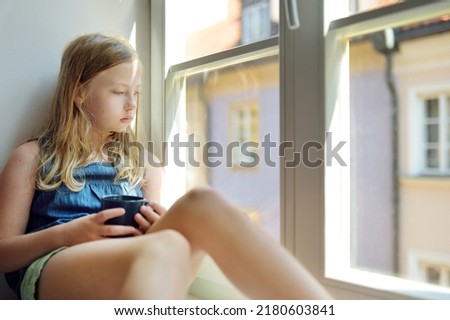 Beautiful preteen girl looking out the window. Young girl sitting on a windowsill. Child admiring city view.