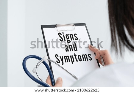 On the table are notepads, a stethoscope, a pen and a sheet of paper with the text SINGS AND SYMPTOMS. Medical concept.