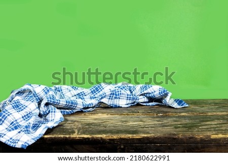 Empty wooden table with plaid tablecloth and wooden board over green background