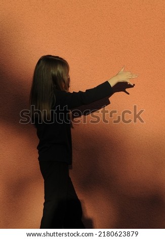 Cute little girl playing in shadow theater on orange color background.