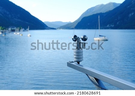 modern device anemometer over alpine lake controls parameters, meteorological equipment measures speed of movement of air masses, humidity levels, atmospheric pressure, wind strength and direction Royalty-Free Stock Photo #2180628691
