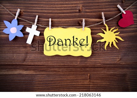 A Yellow Banner with the German Word Danke, which means Thanks, hanging on a Line with different Symbols on Wood