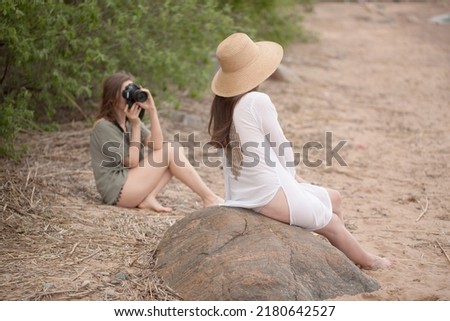 a beautiful brunette girl in a straw hat and a light summer dress poses for a photographer on the beach