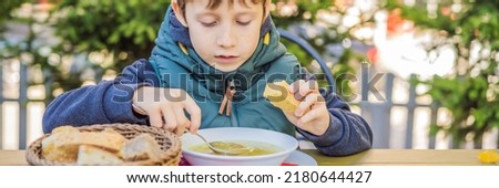 BANNER, LONG FORMAT Adorable little school boy eating vegetable soup outdoor. Blond child in domestic kitchen or in school canteen. Cute kid and healthy food, organic vegan soup with potato, tomato