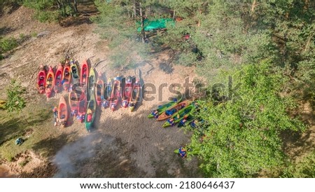 Aerial view of camping with kayaks on the beach of river on a sunny day. Modern kayaks with paddles on beach near river. Summer camp activity. Travel concepts. Nature background.