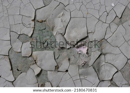 Peeling paint on the wall. Old concrete wall with cracked flaking paint. Weathered rough painted surface with patterns of cracks and peeling. Grunge texture for background and design. High resolution. Royalty-Free Stock Photo #2180670831