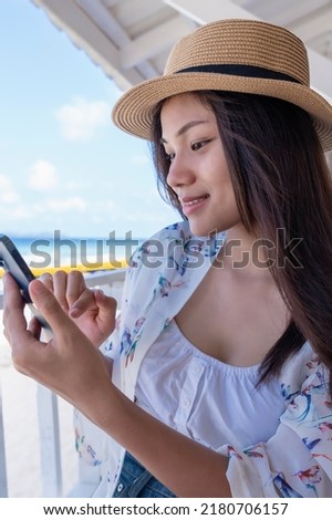 Young woman using smartphone by seaside. Happy tourist relaxing and using mobile phone for social network on beach of tropical sunrise uses communication technology. Travel concepts and technology