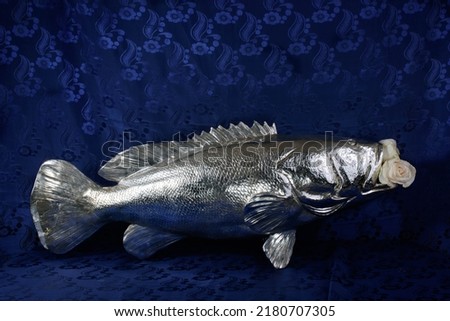 Silver fish with a white rose in it's mouth on a royal blue background