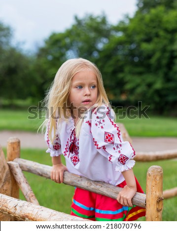 Little girl in ukrainian traditional clothes on the hedge in village