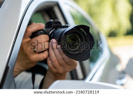A paparazzi sits in his car and takes pictures of a famous person.  Spy with camera in the car. A private detective, sitting inside the car, taking pictures with the camera.