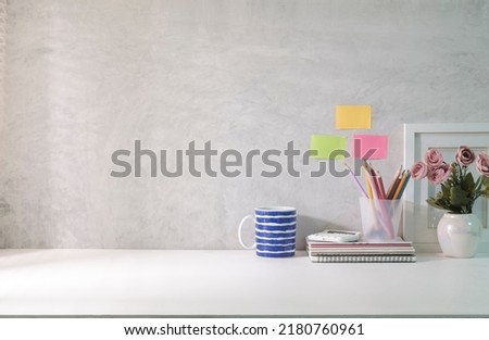 Minimal workplace with empty picture frame, book, coffee cup and pencil holder on white table. Copy space for your text.