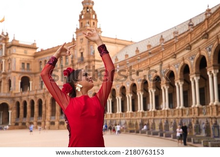 Beautiful teenage woman dancing flamenco in a square in Seville, Spain. She wears a red dress with ruffles and dances flamenco with a lot of art. Flamenco cultural heritage of humanity. Royalty-Free Stock Photo #2180763153