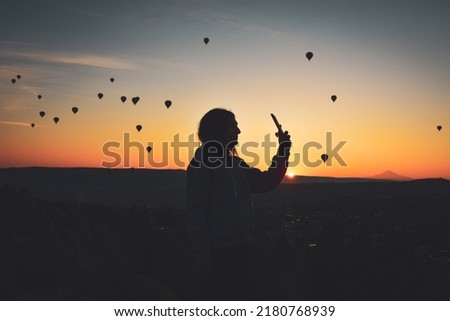 Silhouette of Smart phone in hands of woman taking pictures of a beautiful landscape and balloons in Cappadocia. Sunrise time, dreamy travel concept