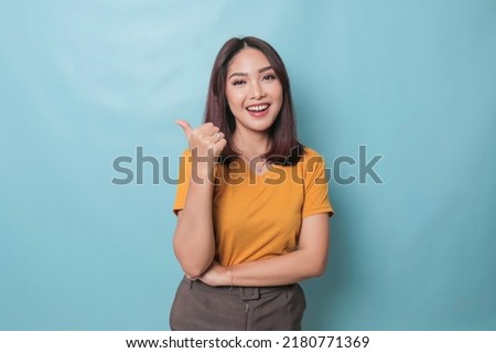 Young pretty woman smiling joyfully and looking happy, feeling carefree and positive with both thumbs up isolated by blue background