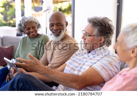 Caucasian senior man using digital pc while sitting with multiracial friends on sofa in nursing home. Wireless technology, happy, togetherness, unaltered, support, assisted living and retirement.