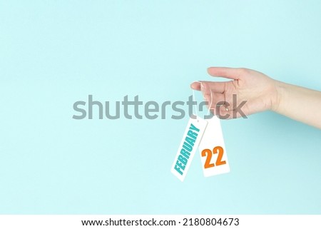 February 22nd. Day 22 of month, Calendar date. Hand hold price tag with calendar date on blue background.  Winter month, day of the year concept