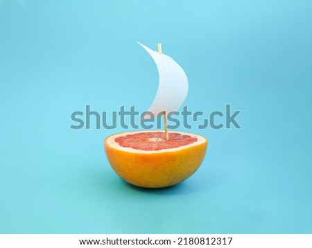 Boat made of grapefruit slice and paper sail against bright blue background. Original grapefruit decoration. Creative summer idea. Minimal style. Fruit concept. Royalty-Free Stock Photo #2180812317