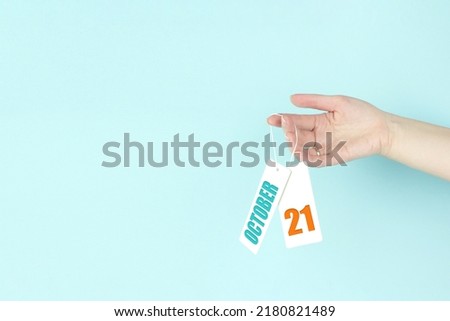 October 21st . Day 21 of month, Calendar date. Hand hold price tag with calendar date on blue background.  Autumn month, day of the year concept