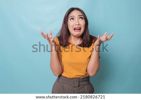beautiful young woman crying feeling very depressed isolated by blue background shouting loud