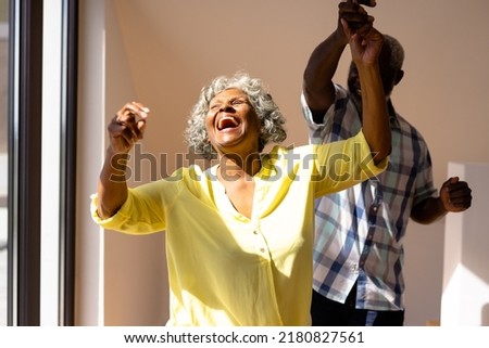 African american senior man dancing with cheerful woman against wall in nursing home. Laughing, friendship, togetherness, enjoyment, unaltered, recreation, support, assisted living and retirement.