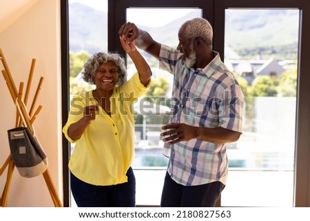 Cheerful african american senior man doing salsa dance with woman against window in nursing home. Friendship, togetherness, enjoyment, unaltered, recreation, support, assisted living and retirement.