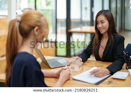 Portrait of an Asian female bank employee asking a customer to read the contract before signing to agree to buy a house, real estate concepts