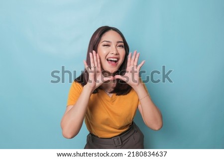 Surprised Asian woman reclines on her hands and shouting while looking at the camera over blue background Royalty-Free Stock Photo #2180834637