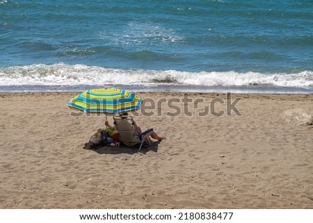 Woman in swimsuit sunbathes sitting in lounge chair near the sea water. Beach vacation on summer resort