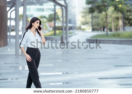 Arab woman walking talking on mobile phone in business background wearing professional. businesswoman looking Indian or Asian calling using her smartphone