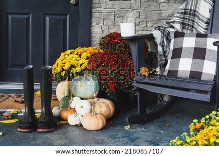 Hot coffee sitting on rocking chair on front porch that has been decorated for autumn with white, orange, grey pumpkins, rain boots and mums. Selective focus with blurred foreground and background. Royalty-Free Stock Photo #2180857107