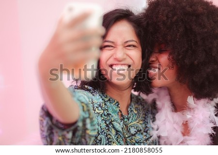 Cheerful female interracial couple taking selfie with smartphone, having fun together