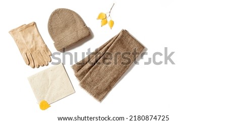 Autumn warm clothes, knitted hat, wool scarf and suede gloves with craft paper for copy space. Warm wear for cold weather in autumnal season. Top view, isolated on white background.
