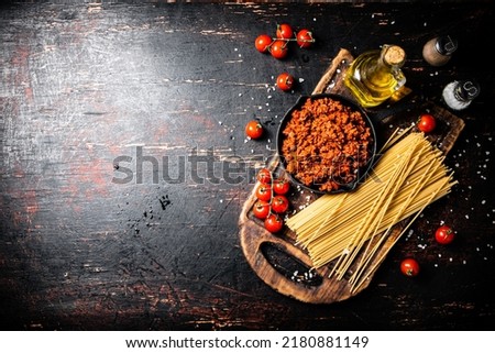 Bolognese sauce on a cutting board with cherry tomatoes and dry pasta. Against a dark background. High quality photo