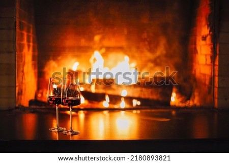 Burning fireplace, close up. Cozy atmosphere autumn or winter evening. Open fire with real flames, firewood burning in fireplace with two glasses of red wine