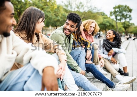 Happy group of trendy young people laughing sitting in city street. Millennial diverse student friends having fun together outdoor Royalty-Free Stock Photo #2180907679