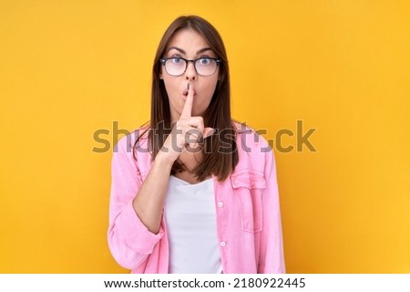 Shh brunette woman asks to keep quiet or secret keeps forefinger on lips isolated on yellow background