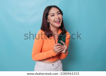 A portrait of a cheerful Asian woman looking at her smartphone over blue background