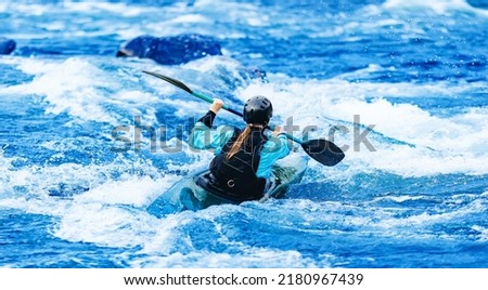 Whitewater kayaking, extreme sport rafting. Young woman in kayak sails mountain river. Royalty-Free Stock Photo #2180967439