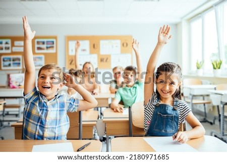 School children in classroom at lesson. Little children raising hands up and having fun in class. Royalty-Free Stock Photo #2180971685