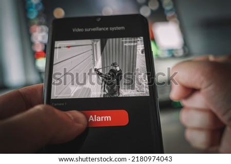Protection of private residential building with help of an external video surveillance system. an application on smartphone screen. CCTV view of burglar breaking into home through window with crowbar. Royalty-Free Stock Photo #2180974043
