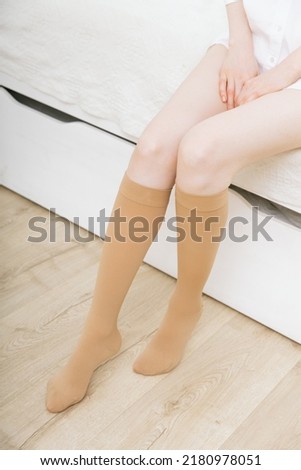 Beige compression stockings on a woman in a white room. Knee socks or socks. Girl putting on stockings at home. Beautiful female legs.