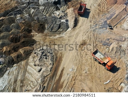 Aerial shot of heavy machinery on construction site or quarry. Drone flying over trucks unloading materials.