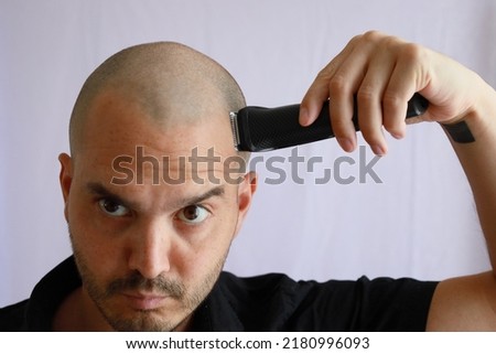 white average bald man shaving his head with an electric razor Royalty-Free Stock Photo #2180996093